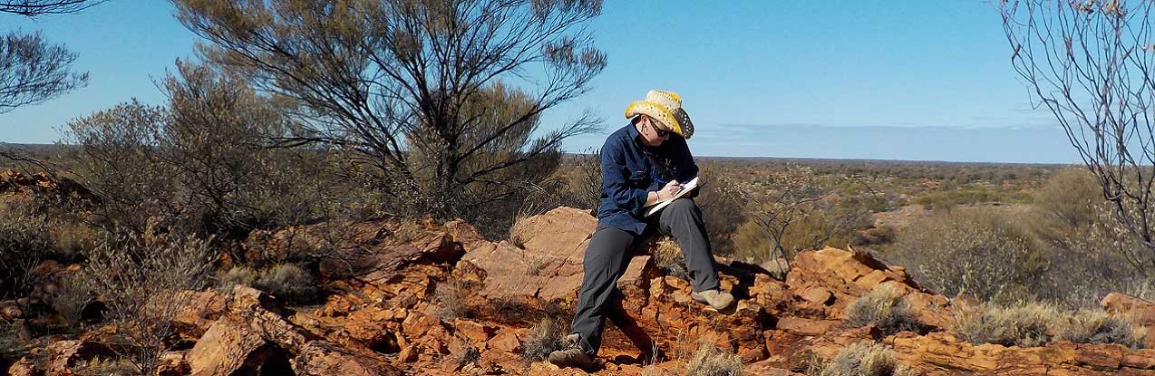 Lady sitting on rocks writing on notepad.